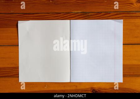 Ein leeres Schulnotizbuch in einem Käfig liegt auf einem hölzernen Schreibtisch, Nahaufnahme, Platz für Text Stockfoto