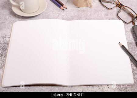 Ansicht eines Notizbuchs von oben mit leeren Seiten, Gläsern, Kaffeetassen und Bleistiften Stockfoto
