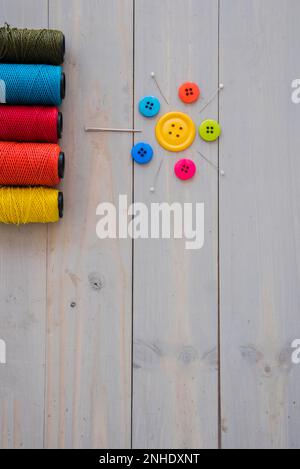 Bunte Garnspulen mit dekorativen Nadeln Stecknadeln bunte Knöpfe Holzschreibtisch Stockfoto