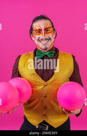 Porträt eines Clowns mit weißer Gesichtsschminke auf pinkfarbenem Hintergrund, jonglierende Bälle Stockfoto