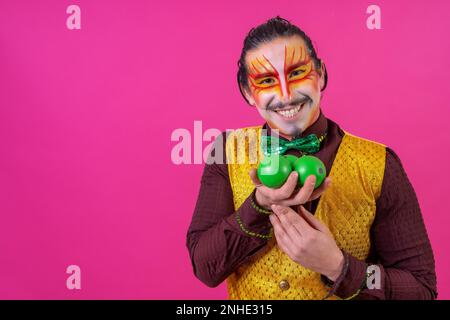 Clown mit weißer Gesichtsschminke auf pinkfarbenem Hintergrund, jonglierende grüne Bälle Stockfoto