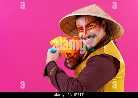 Clown mit weißer Gesichtsschminke auf pinkfarbenem Hintergrund, lächelnd mit Spielzeugpistolen Stockfoto