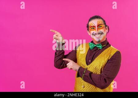 Ein Clown mit weißer Gesichtsschminke, der einen leeren Bereich vor dem pinkfarbenen Hintergrund zeigt und etwas ankündigt Stockfoto