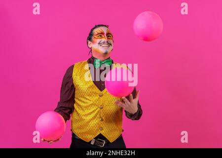 Clown mit weißer Gesichtsschminke auf pinkfarbenem Hintergrund, jonglierende Bälle Stockfoto