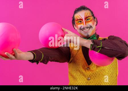 Clown mit weißer Gesichtsschminke auf pinkfarbenem Hintergrund, jonglierende Bälle Stockfoto