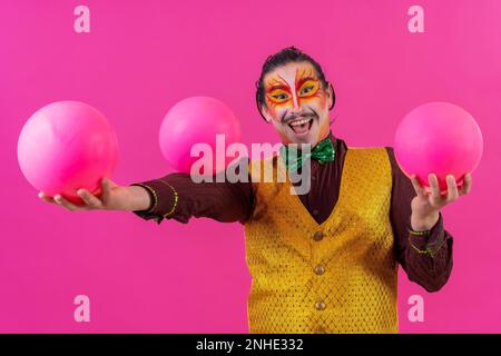 Clown mit weißer Gesichtsschminke auf pinkfarbenem Hintergrund, jonglierende Bälle Stockfoto