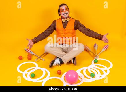 Porträt eines Jongleurs in einer Weste und Make-up mit den jonglierenden Objekten auf gelbem Hintergrund Stockfoto