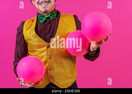 Clown mit weißer Gesichtsschminke auf pinkfarbenem Hintergrund, jonglierende Bälle Stockfoto