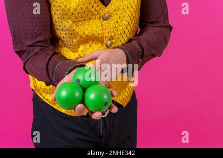 Porträt eines Clowns mit weißer Gesichtsschminke auf pinkfarbenem Hintergrund, mit grünen Bällen jonglierend Stockfoto