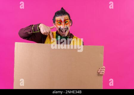 Clown mit weißer Gesichtsmaske, mit einem Schild auf pinkfarbenem Hintergrund, mit der Spitze Stockfoto