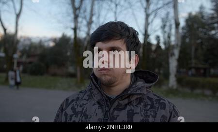 Ein gestresster junger, attraktiver Mann in einer Jacke, der draußen wegschaut und seufzt Stockfoto