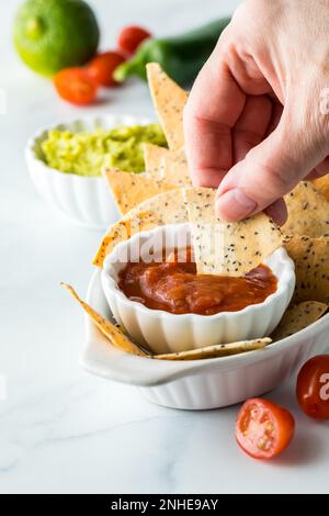 Nahaufnahme einer Hand, die eine Keto-Diät, gebackene Tortilla-Chips in eine Schüssel Salsa taucht. Stockfoto