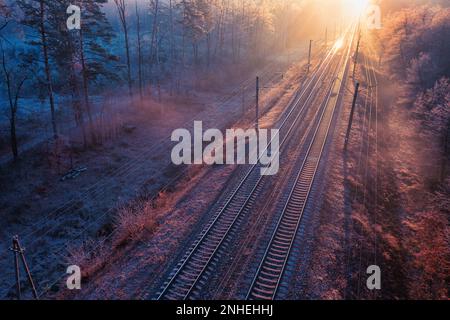 An diesem kühlen Herbstmorgen schlängelt sich die Eisenbahnlinie durch die Wälder. Die Sonnenstrahlen brechen durch die Baumkronen und erhellen die Rostbildung R. Stockfoto