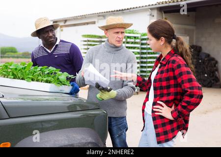 Mädchenmanagerin, die mit Arbeitern die Lieferung von Setzlingen auf die Farm diskutiert Stockfoto
