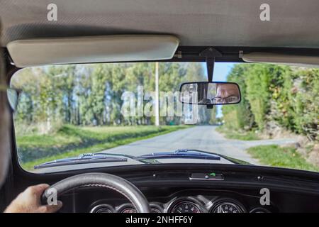 Ein Mann mittleren Alters mit Brille, fährt einen alten Mini-Copper auf dem Land Frankreichs. Fantastisches Wetter aus dem Inneren des Autos Stockfoto