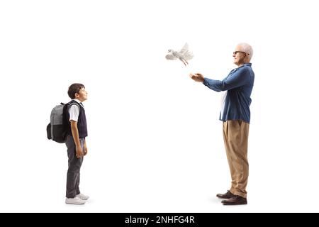 Profilaufnahme eines Schuljungen, der einen Mann beobachtet, der eine weiße Taube auf weißem Hintergrund fliegen lässt Stockfoto