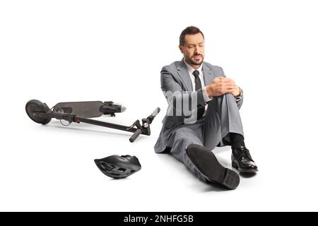 Geschäftsmann mit einem elektrischen Roller, der auf dem Boden sitzt und sein verletztes Knie isoliert auf weißem Hintergrund hält Stockfoto