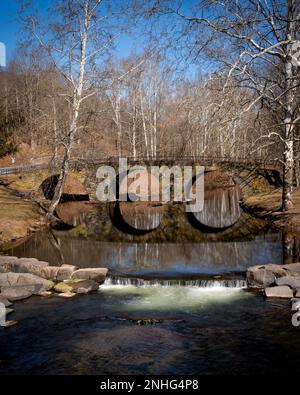 Kenoza Lake, NY - USA - 20. Februar 2023 Vertikaler Blick auf die malerische Stone Arch Bridge mit drei Bogenbögen, die sich über den East Branch des Callicoon erstreckt Stockfoto