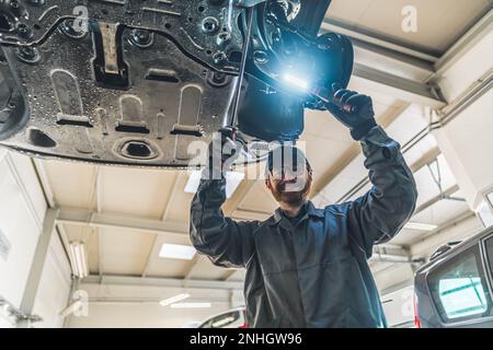 Schuss aus niedrigem Winkel. Ein Mechaniker, der das Fahrgestell des Fahrzeugs überprüft und direkt in die Kamera schaut. Hochwertiges Foto Stockfoto