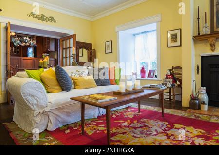 Teakholz Couchtisch, Sofa mit bunten Kissen im Wohnzimmer mit französischen Türen, die in die Küche im alten Haus aus dem Jahr 1830 führen. Stockfoto
