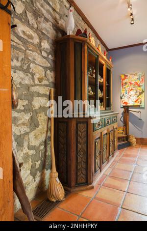 Handgeschnitztes Holzbuffet vor einer alten Felssteinwand im Speisesaal mit Terrakotta-Keramikfliesen im alten Haus aus dem Jahr 1830. Stockfoto