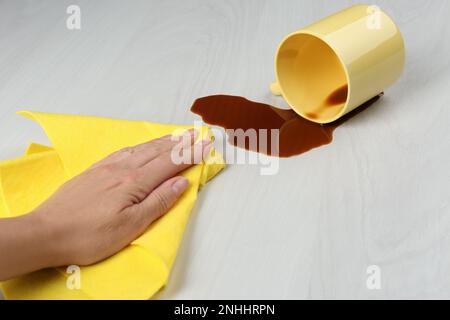 Eine Frau, die verschütteten Kaffee auf einem weißen Holztisch aufräumte, machte eine Nahaufnahme Stockfoto