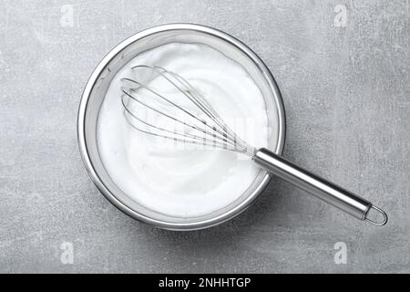 Eiweiß mit Schneebesen auf grauem Tisch, Draufsicht Stockfoto