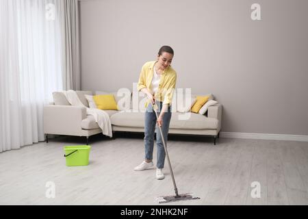 Junge Frau, die den Boden mit Mopp im Wohnzimmer putzt Stockfoto