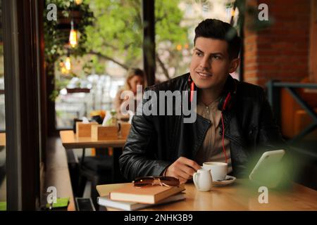 Mann mit Kopfhörern und Smartphone am Tisch im Café Stockfoto