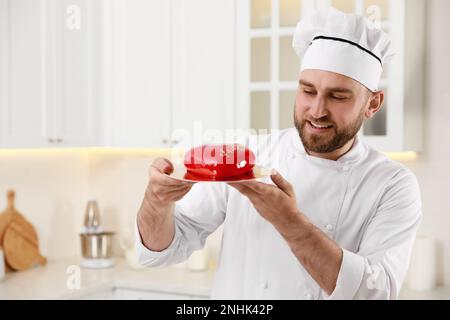 Glücklicher professioneller Konditor, der köstlichen Kuchen in der Küche hält Stockfoto