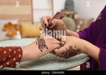 Professioneller Mehndi-Meister, der Henna-Tattoo drinnen macht, Nahaufnahme Stockfoto