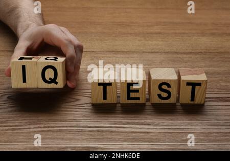 Mann nimmt Würfel mit Text IQ Test auf Holz Hintergrund, Nahaufnahme Stockfoto