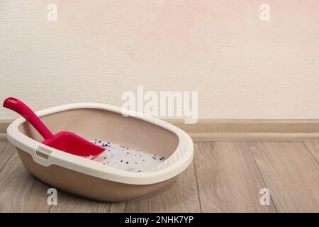 Katzenschale mit Kristallstreu und Schaufel auf dem Boden nahe der rosafarbenen Wand. Platz für Text Stockfoto