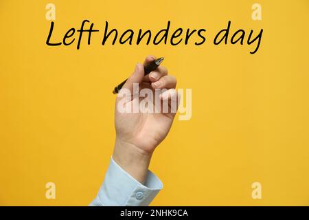 Eine Linkshänderin hält einen Stift auf gelbem Hintergrund, Nahaufnahme Stockfoto