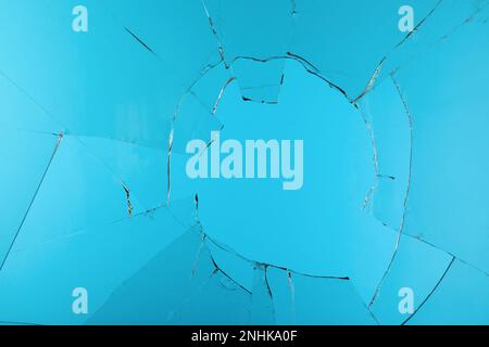 Nahaufnahme von zerbrochenem Glas mit Rissen auf hellblauem Hintergrund Stockfoto
