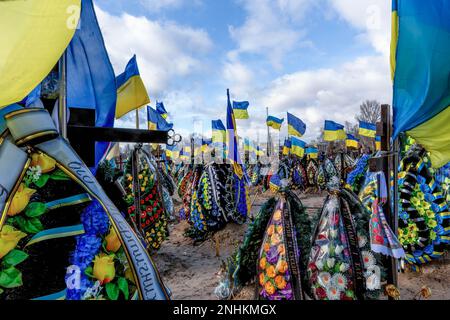 Blaue und gelbe ukrainische Nationalflaggen werden vom Wind geweht, und Blumen liegen auf Gräbern von Soldaten, die im Kampf gegen russische Streitkräfte getötet wurden, auf dem Friedhof von Lisove in der Hauptstadt der Ukraine. Da sich die Invasion der Ukraine durch die russischen Streitkräfte ihrem ersten Jahrestag nähert, ist die Zahl der Opfer sehr hoch, obwohl die genauen Zahlen unbekannt sind. Mindestens 13 ukrainische Soldaten haben ihr Leben verloren. Stockfoto