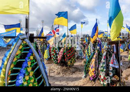 Blaue und gelbe ukrainische Nationalflaggen werden vom Wind geweht, und Blumen liegen auf Gräbern von Soldaten, die im Kampf gegen russische Streitkräfte getötet wurden, auf dem Friedhof von Lisove in der Hauptstadt der Ukraine. Da sich die Invasion der Ukraine durch die russischen Streitkräfte ihrem ersten Jahrestag nähert, ist die Zahl der Opfer sehr hoch, obwohl die genauen Zahlen unbekannt sind. Mindestens 13 ukrainische Soldaten haben ihr Leben verloren. Stockfoto