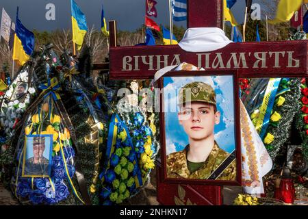 Porträts gefallener Soldaten neben blauen und gelben ukrainischen Nationalflaggen und Blumen liegen auf Gräbern von Soldaten, die im Kampf gegen russische Streitkräfte getötet wurden, auf dem Lisove Friedhof in der Hauptstadt der Ukraine. Da sich die Invasion der Ukraine durch die russischen Streitkräfte ihrem ersten Jahrestag nähert, ist die Zahl der Opfer sehr hoch, obwohl die genauen Zahlen unbekannt sind. Mindestens 13 ukrainische Soldaten haben ihr Leben verloren. Stockfoto