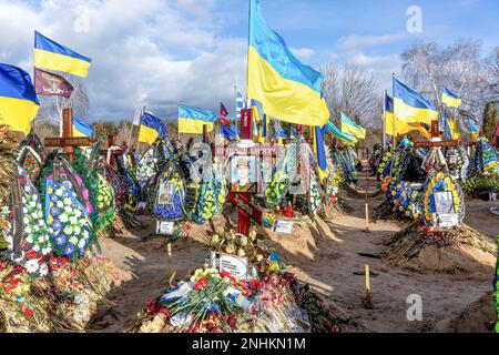 Blaue und gelbe ukrainische Nationalflaggen werden vom Wind geweht, und Blumen liegen auf Gräbern von Soldaten, die im Kampf gegen russische Streitkräfte getötet wurden, auf dem Friedhof von Lisove in der Hauptstadt der Ukraine. Da sich die Invasion der Ukraine durch die russischen Streitkräfte ihrem ersten Jahrestag nähert, ist die Zahl der Opfer sehr hoch, obwohl die genauen Zahlen unbekannt sind. Mindestens 13 ukrainische Soldaten haben ihr Leben verloren. Stockfoto