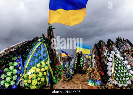 Kiew, Oblast Kiew, Ukraine. 21. Februar 2023. Blaue und gelbe ukrainische Nationalflaggen werden vom Wind geweht, und Blumen liegen auf Gräbern von Soldaten, die im Kampf gegen russische Streitkräfte getötet wurden, auf dem Friedhof von Lisove in der Hauptstadt der Ukraine. Da sich die Invasion der Ukraine durch die russischen Streitkräfte ihrem ersten Jahrestag nähert, ist die Zahl der Opfer sehr hoch, obwohl die genauen Zahlen unbekannt sind. Mindestens 13 ukrainische Soldaten haben ihr Leben verloren. (Kreditbild: © Dominika Zarzycka/SOPA Images via ZUMA Press Wire) NUR REDAKTIONELLE VERWENDUNG! Nicht für den kommerziellen GEBRAUCH! Stockfoto