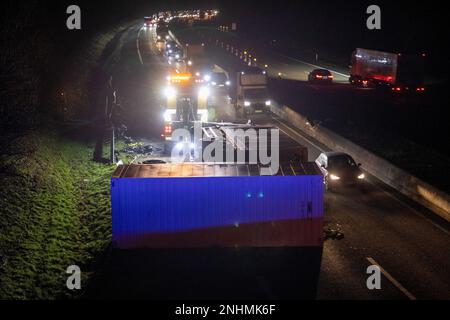 Burghaun, Deutschland. 21. Februar 2023. Ein Lkw wird nach einem Unfall auf der Autobahn 7 (A7) umgestürzt. Bei einem Lkw-Unfall auf der Autobahn 7 nahe Burghaun (Bezirk Fulda) wurde ein Lkw-Fahrer leicht verletzt. Der 44-Jährige kippte mit seinem Anhänger um, nachdem er die Straße verlassen hatte, gab die Polizei in der Nacht bis Mittwoch bekannt. Die A7 wurde wegen des Unfalls in Richtung Kassel geschlossen, später wurde die linke Spur geöffnet. Kredit: Fuldamedia/dpa/Alamy Live News Stockfoto