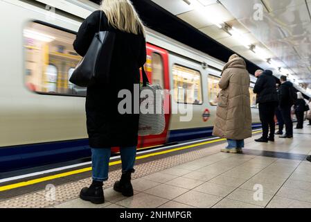 Passagiere, die auf dem Londoner U-Bahnsteig warten, mit der U-Bahn, die am Bahnhof ankommt. Bahnhof Westminster. Weiblich mit Taschen Stockfoto