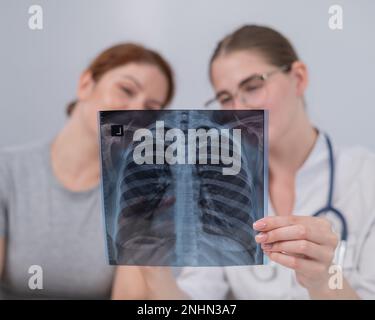 Der Arzt konsultiert eine kaukasische Frau und kommentiert die Röntgenaufnahme der Lunge. Stockfoto