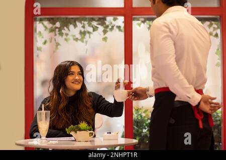 Junge Frau, die die Rechnung vom Kellner im Café annimmt Stockfoto