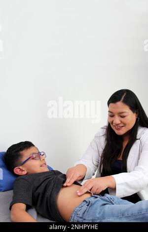 Eine lateinische Ärztin prüft den Bauch eines Kindes in ihrer Praxis, um Krankheiten wie Blinddarmentzündung, Gastroenteritis, Hernie oder Geschwür auszuschließen Stockfoto