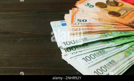 Nahaufnahme des Bündels von Euro-Banknoten und -Münzen auf schwarzem Holzhintergrund Stockfoto