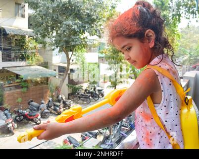 Süßes kleines indisches Mädchen spielt Farben auf dem Holi Festival, hält ein Pichakaree voller Farben, Holi Festivalfeiern in Delhi, Indien Stockfoto