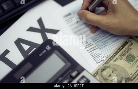 Das Konzept der Steuersaison. Frau füllt das US-Einkommensteuerformular für die Steuerzahlung manuell aus. Geld und Finanzkonzept. Papierkram für die Zahlung von Steuern. Stockfoto