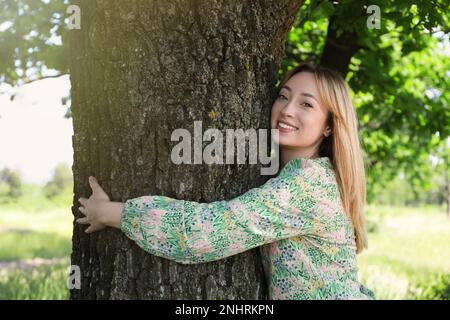 Schöne junge Frau, die im Wald Baumstämme umarmt Stockfoto