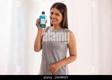 Lächelnde Frau mit einer Flasche Mundwasser vor weißem Hintergrund Stockfoto